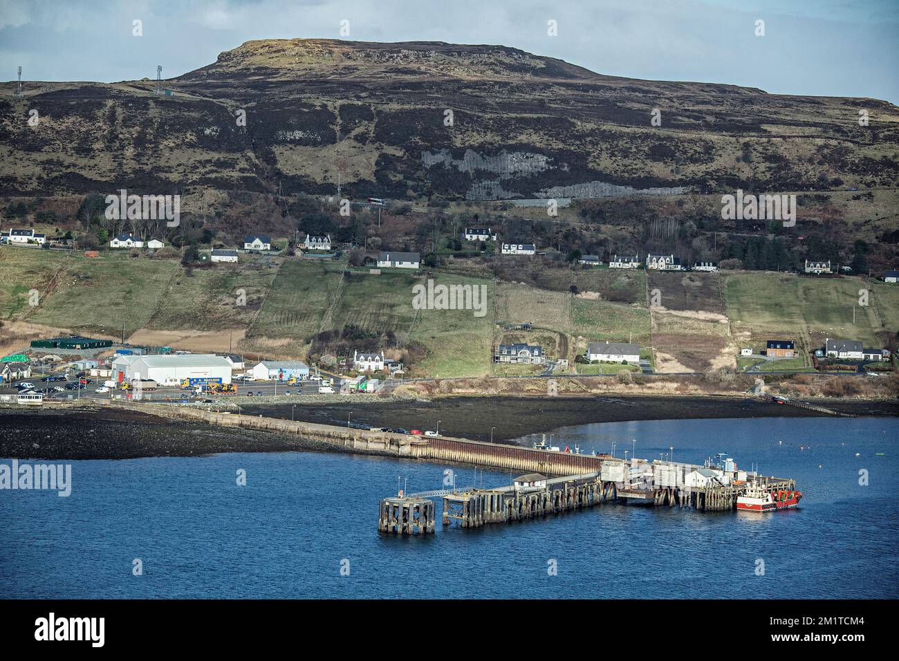 A boat alongside the Jetty at Uig, Isle of Skye, with the village and Cuillin hills behind. Stock Photo