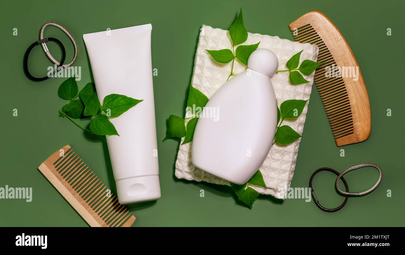 Natural Hair cosmetics. Hair care flat lay with shampoo and conditioner bottles with combs and towel on a green background. Mock up of organic beauty Stock Photo