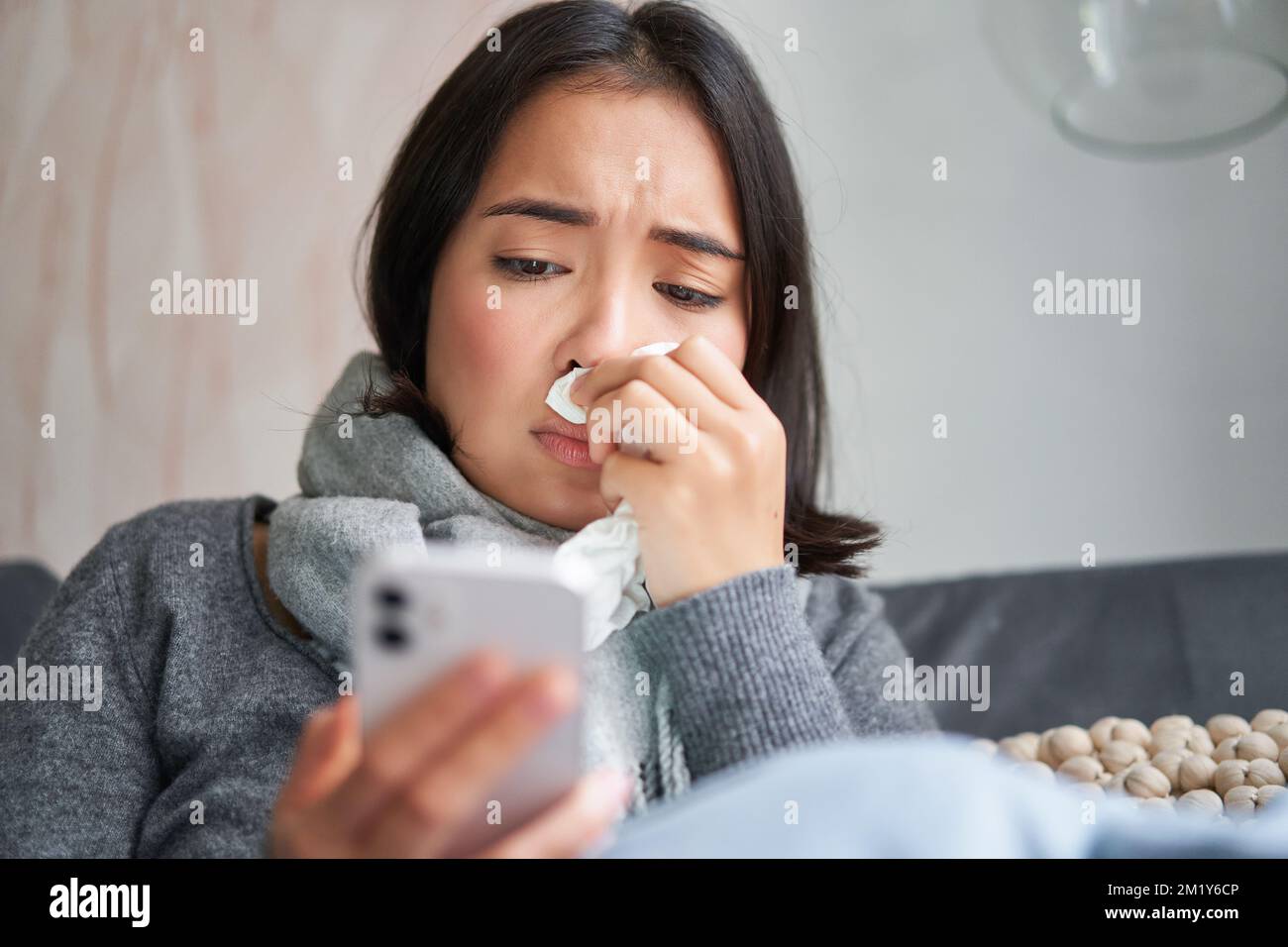 Ill korean woman sitting at home, sneezing, caught cold, reading news