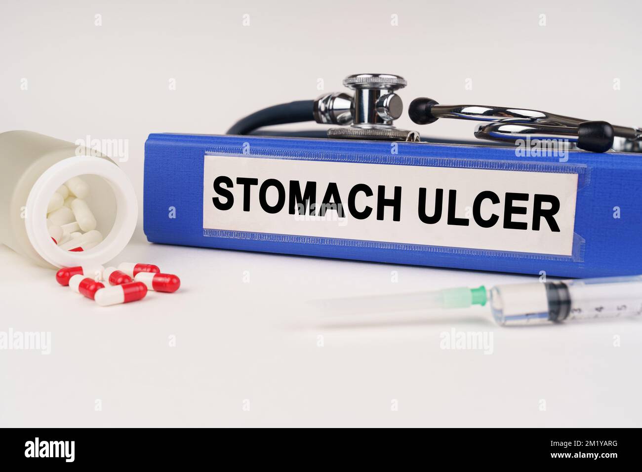 Medical concept. On a white surface there are pills, a syringe, a stethoscope and a folder with the inscription - Stomach ulcer Stock Photo
