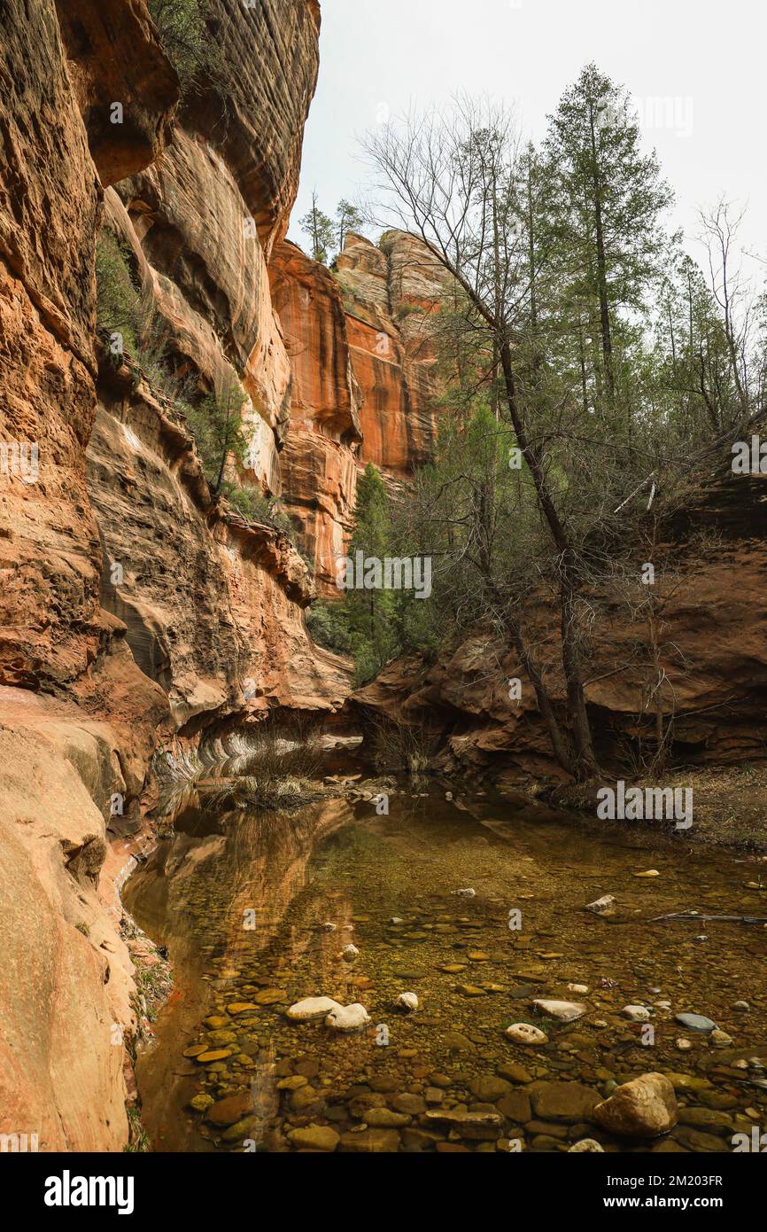 A river flowing beside a cliff of a tall, red rock Stock Photo
