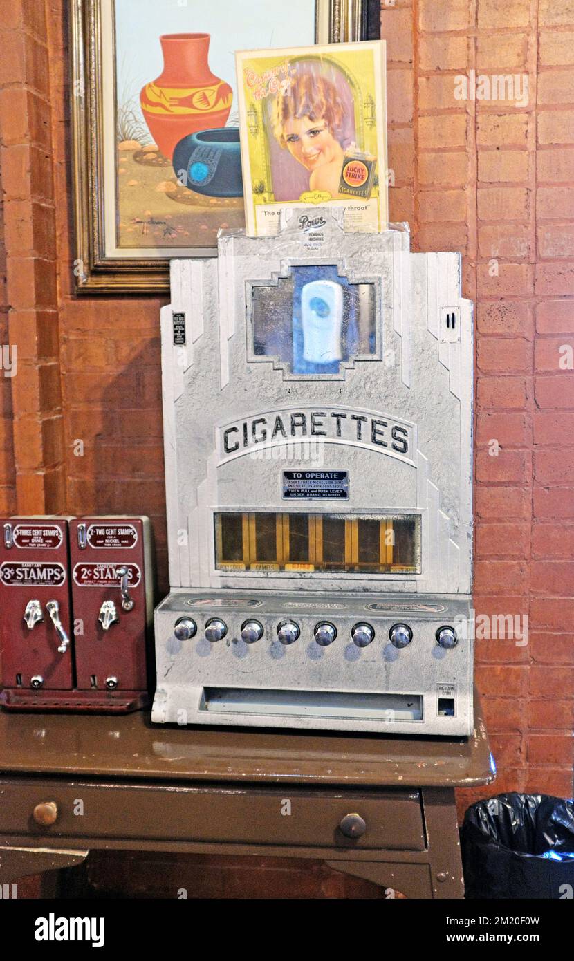 An antique tabletop cigarette vending dispenser next to vintage stamp machines. Stock Photo