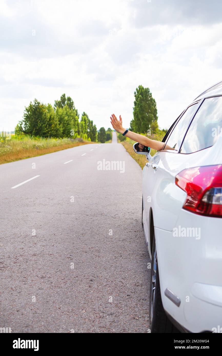 A young girl driving a car pulling her hand out of the window stops the