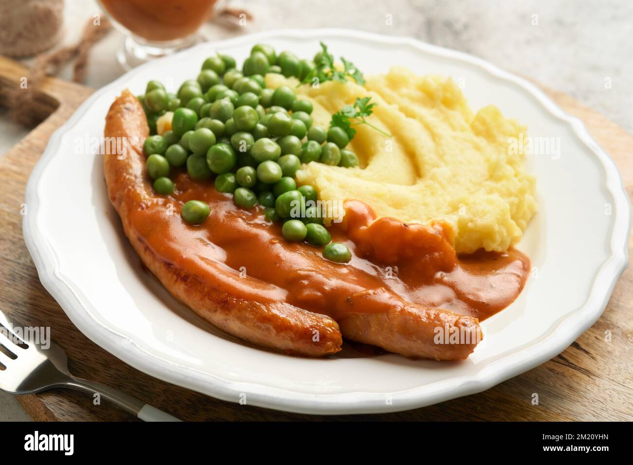 Bangers and mash. Grilled sausages with mash potato and green pea on white plate on grey background. Traditional dish of Great Britain and Ireland. BB Stock Photo