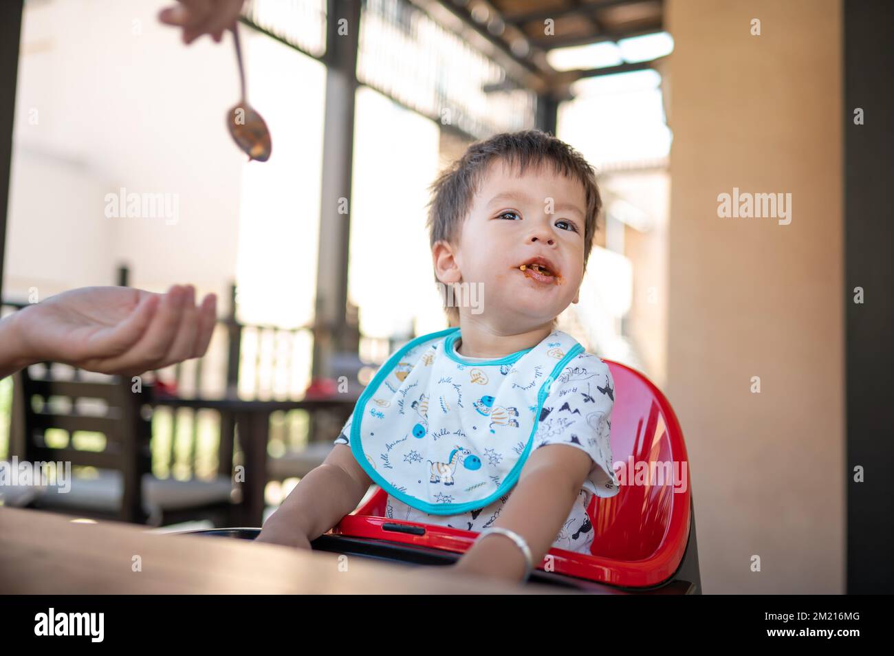 Toddler sitting on a high chair in the restaurant during a meal. Handsome multiracial one and half year old baby boy having a dinner meal in the resta Stock Photo