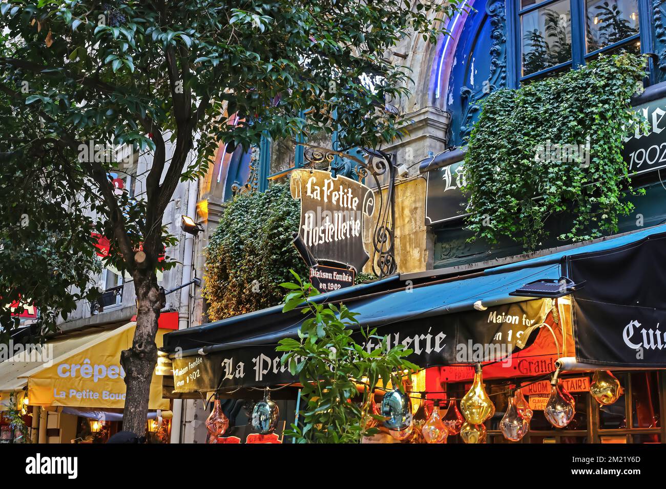 Paris (Quartier Latin), France - November 9. 2022: Beautiful colorful old romantic vintage restaurant at night, green trees and plants, awning Stock Photo
