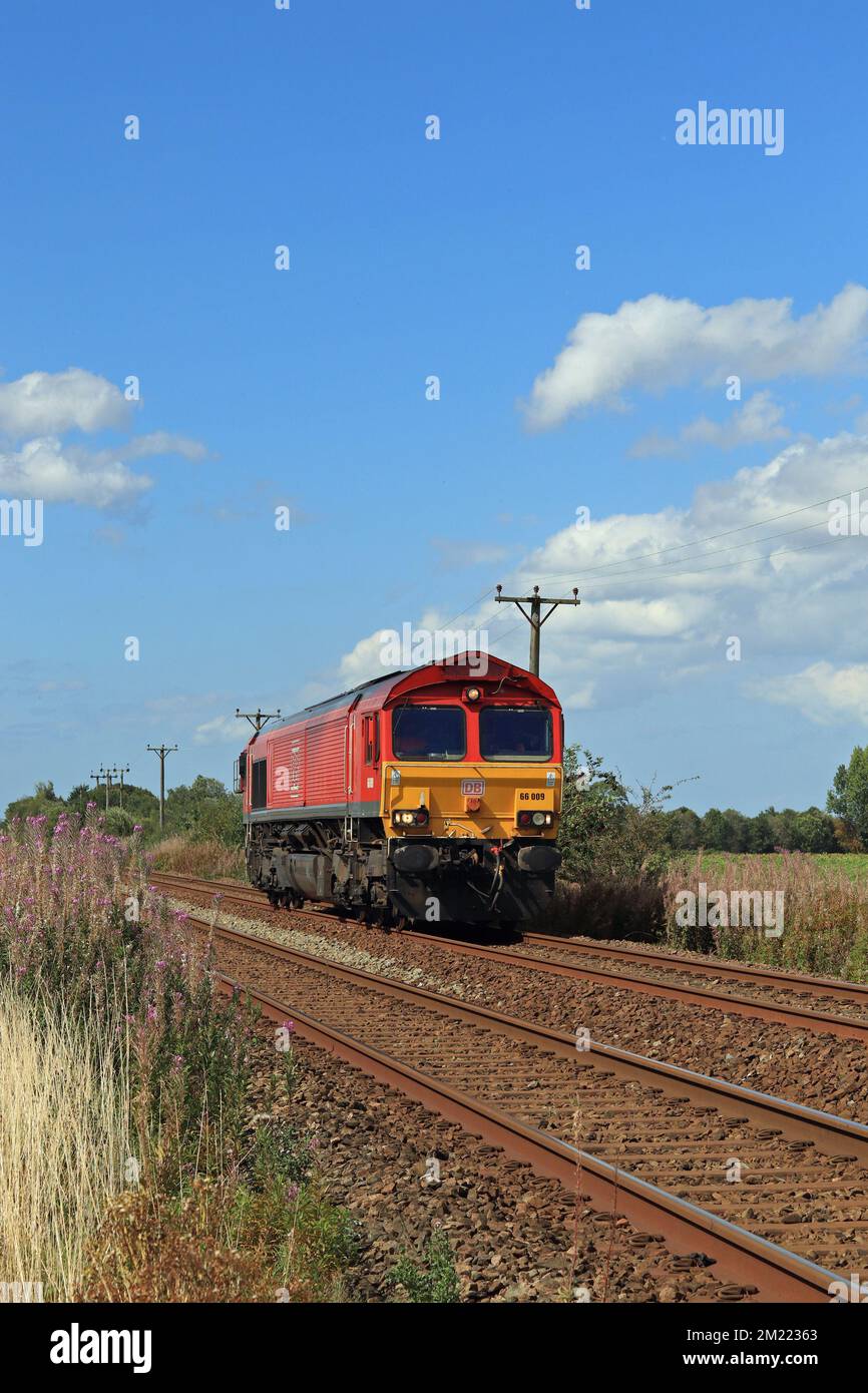Under the wide blue skies of West Lancashire DB Cargo diesel locomotive 66009 approaches a pedestrian foot crossing on Burscough Moss. Stock Photo