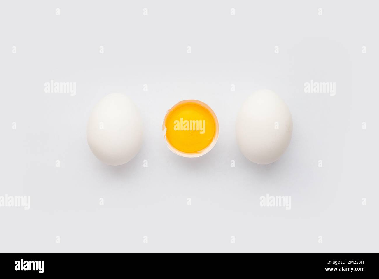 Whole chicken Eggs and cracked half with yolk on white background. Minimalism Stock Photo
