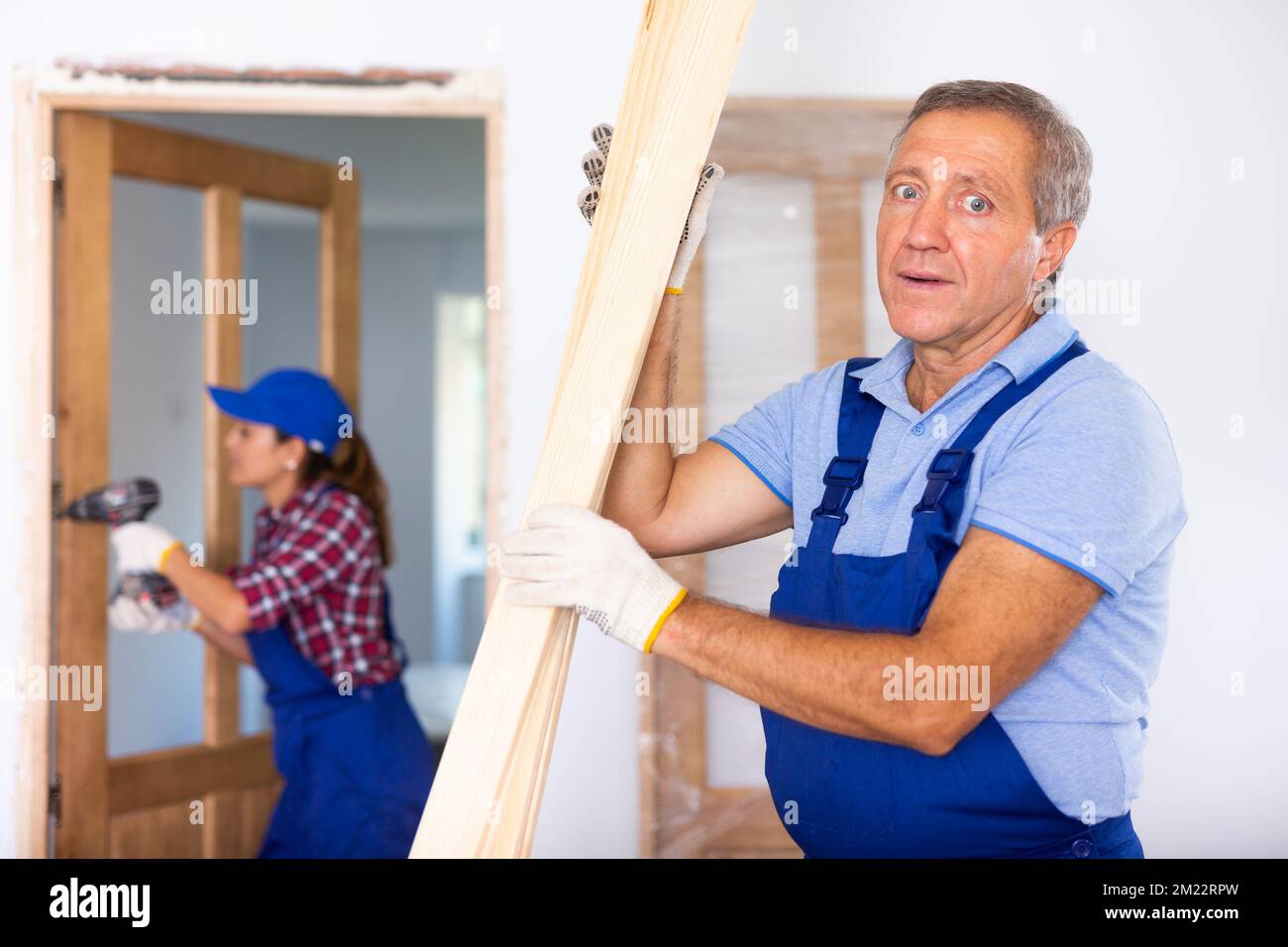 Confident middle-aged repairman in uniform checking wooden timber at a construction site in an apartment Stock Photo
