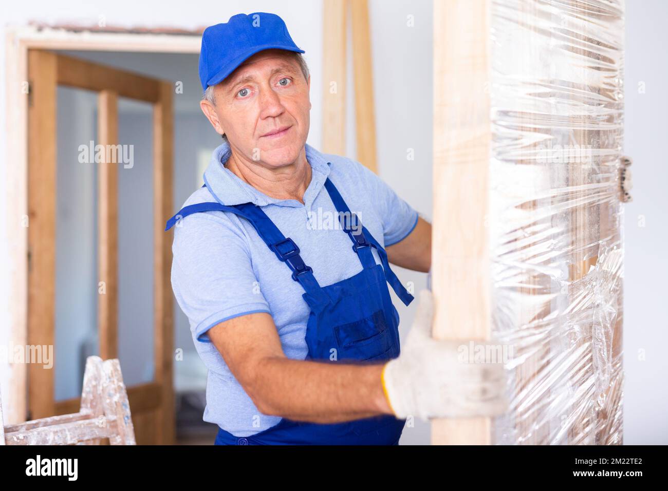 Professional male craftsman in overalls dragging the door construction into an apartment Stock Photo