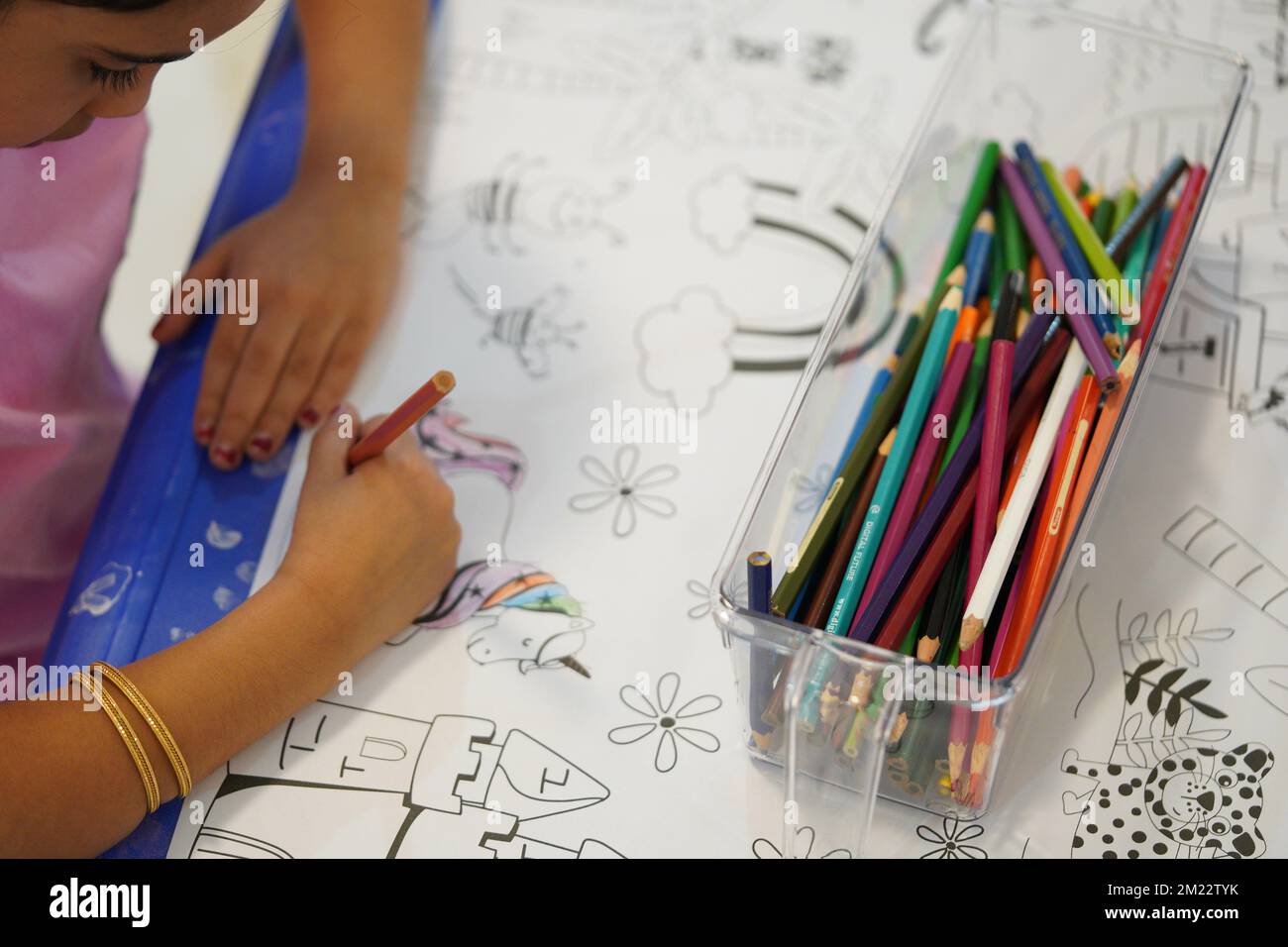 A child sits and colours a giant colouring paper pattern. Child holds a pencil in his hand. A set of coloured pencils on a box. Drawing activities. Stock Photo