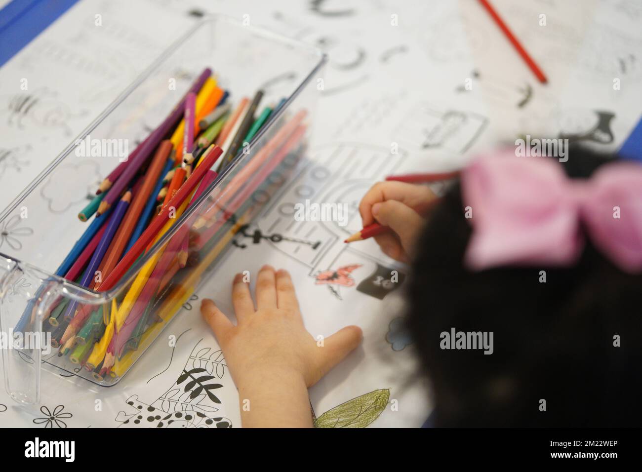 A child sits and colours a giant colouring paper pattern. Child holds a pencil in his hand. A set of coloured pencils on a box. Drawing activities. Stock Photo