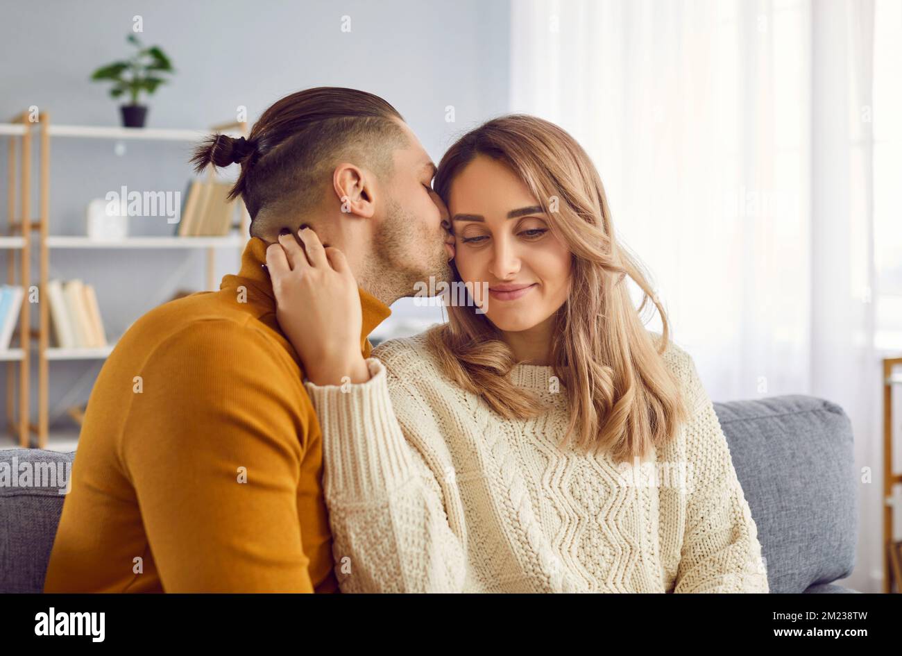 Portrait of handsome husband who gently kissing his attractive wife in cheek at home in morning. Stock Photo