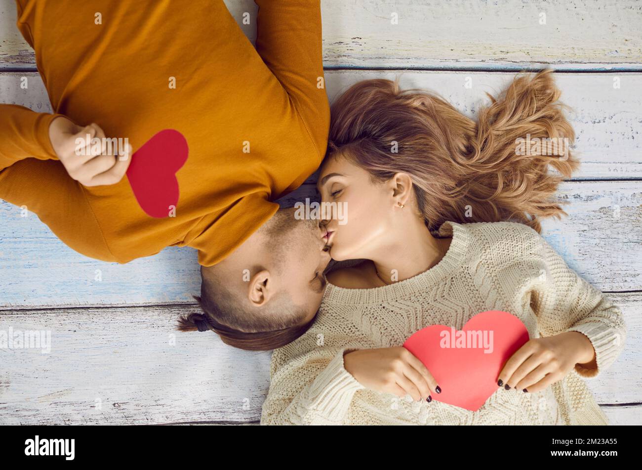 Young couple in love are kissing lying on floor with valentine hearts in their hands. Stock Photo