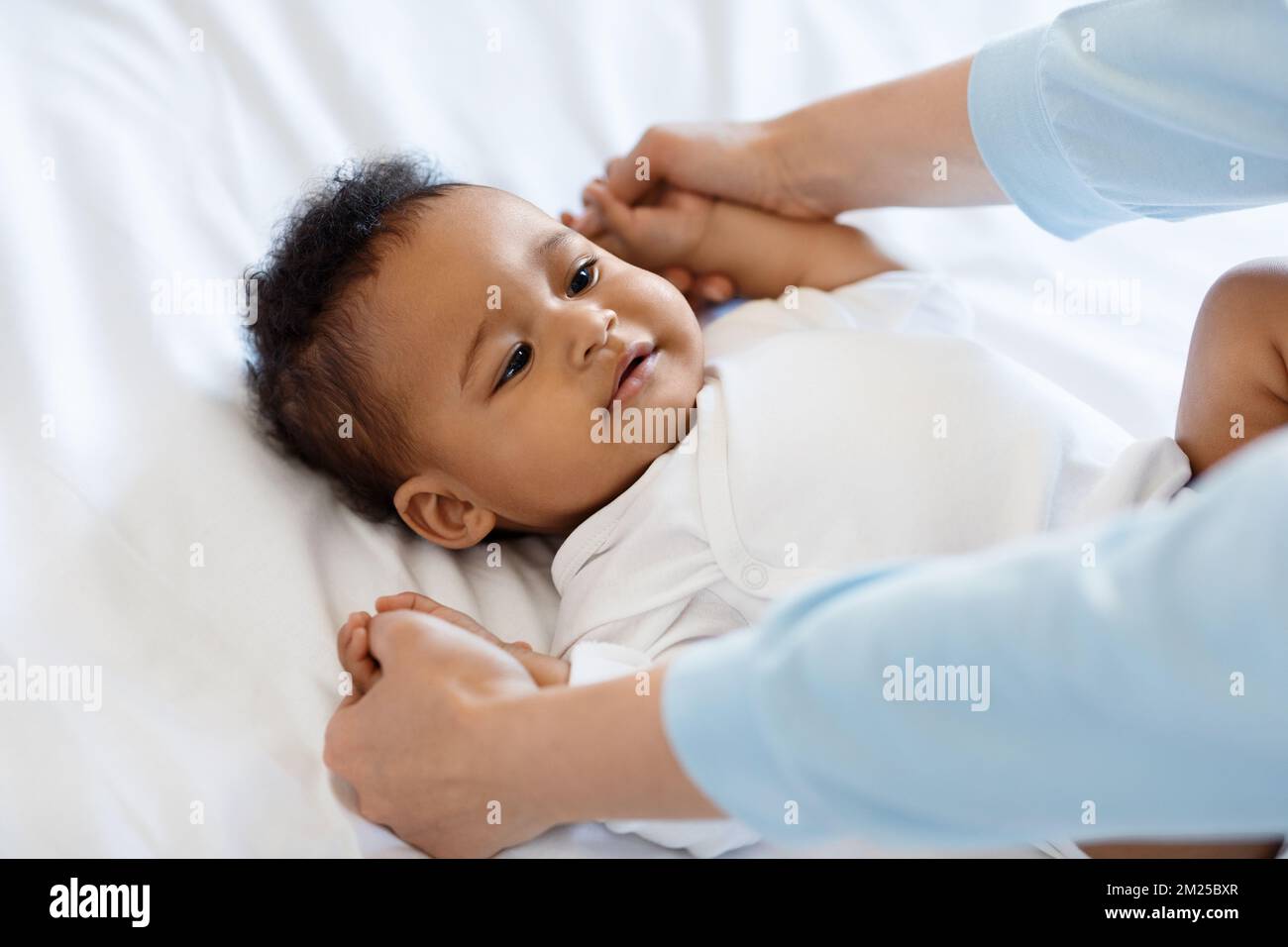 Unrecognizable Mother Making Gymnastics With Cute Little Black Baby Lying On Bed Stock Photo