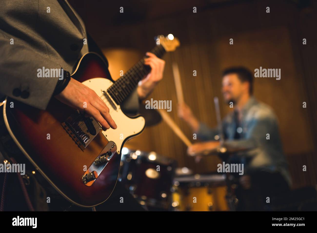 Band concert concept. Unrecognizable person playing electric guitar in the foreground. Blurred drummer in the background. High quality photo Stock Photo
