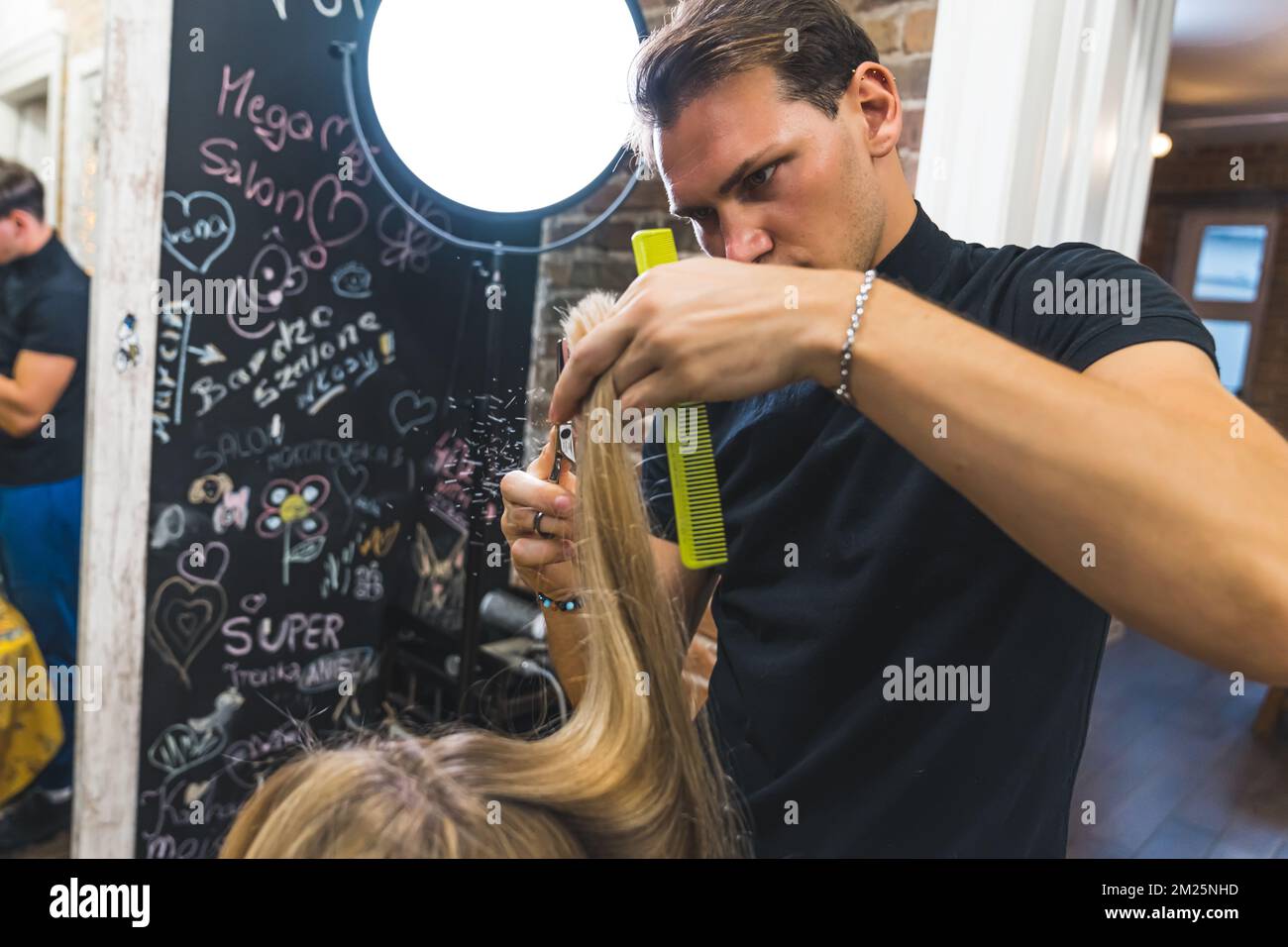 Male hairdresser cutting long blonde hair of a woman with scissors. High quality photo Stock Photo