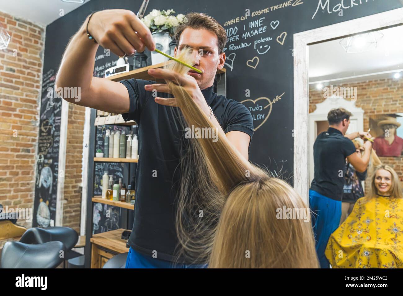 Male hairdresser cutting long blonde hair of a woman with scissors. High quality photo Stock Photo