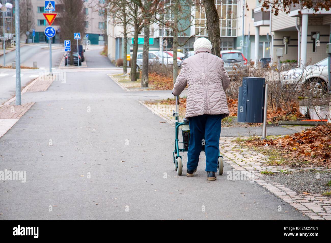 An elderly woman walking with a wheeled walker on an empty street in ...