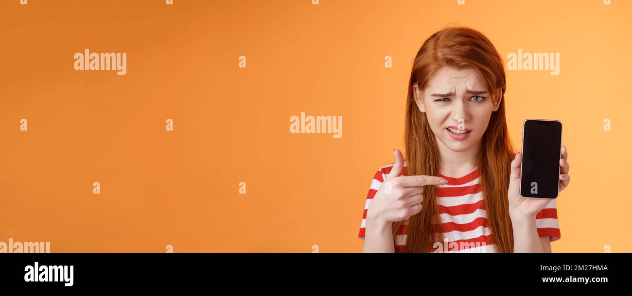 Perplexed disappointed redhead girl show smartphone screen app
