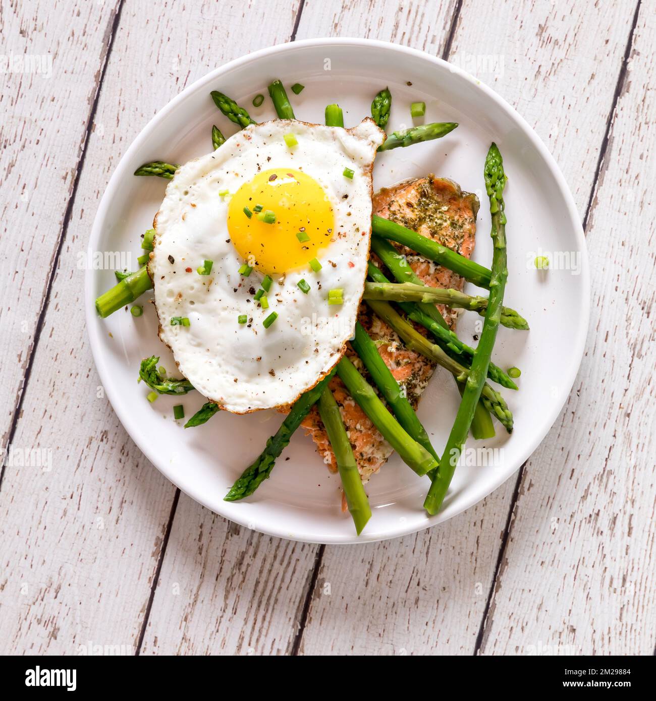 A plate of roasted salmon, sauteed asparagus and a fried egg on top. Stock Photo