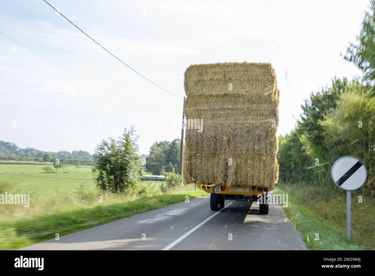 Tractor loaded with bales of straw on a countryside road | Tracteur charge de bottes de paille sur une route de campagne 29/08/2017 Stock Photo