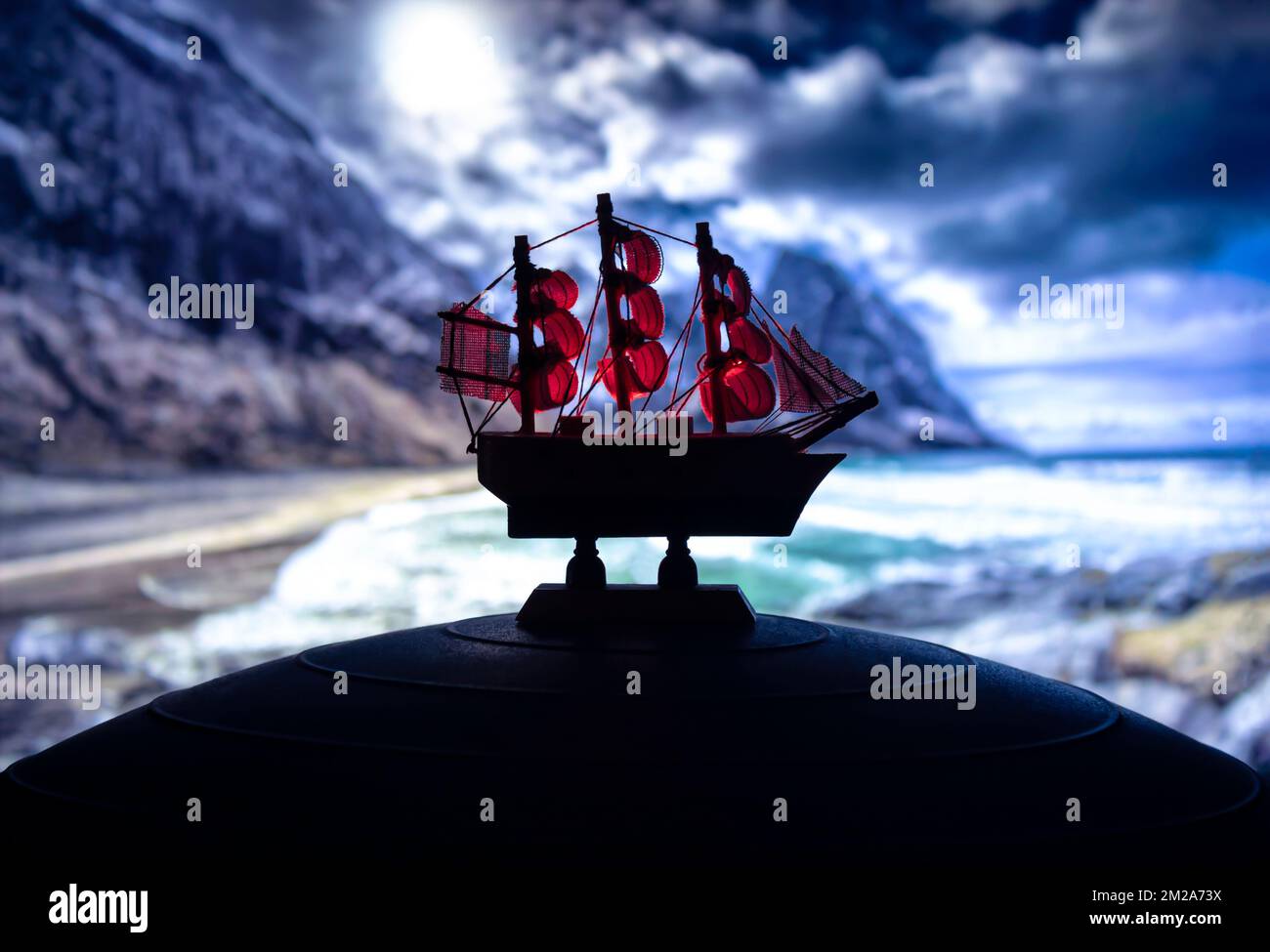 Beautiful boat toy over a blue balll with blurred night beach scene at background. Travel, adventrure, and nature concept Stock Photo