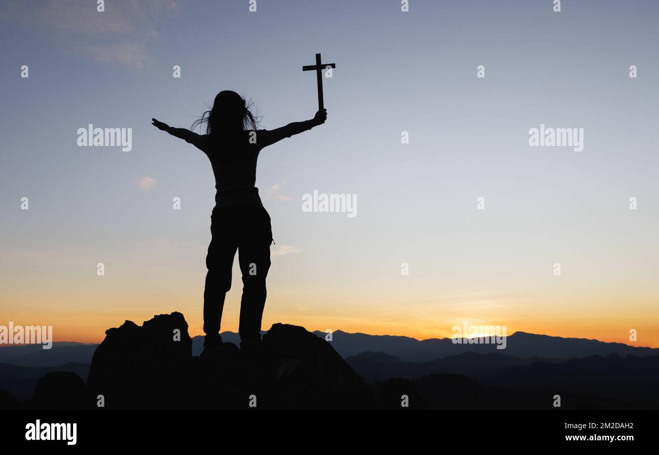 Silhouette of christian young woman praying with a cross at sunrise ...