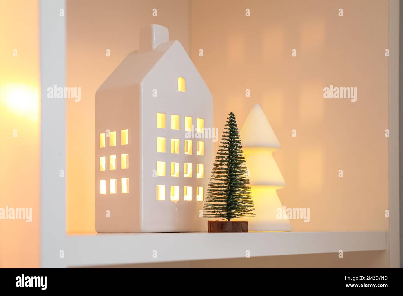 House shaped candle holder and Christmas trees on shelf, closeup Stock