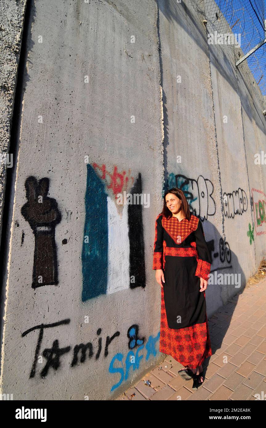 A Palestinian woman standing by barrier built by the Israeli government. The wall is painted with the Palestinian flag. Stock Photo