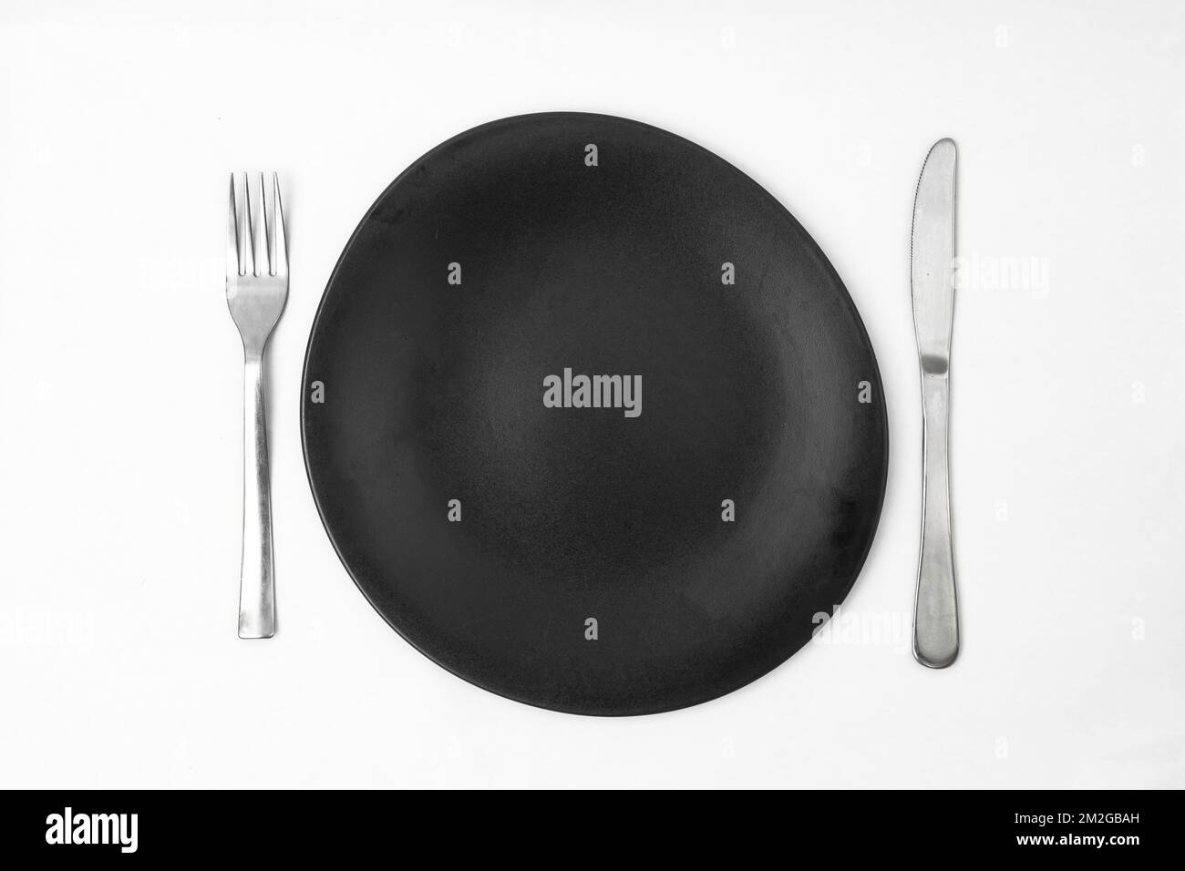 irregular round black plate with silver fork and knife on white background Stock Photo