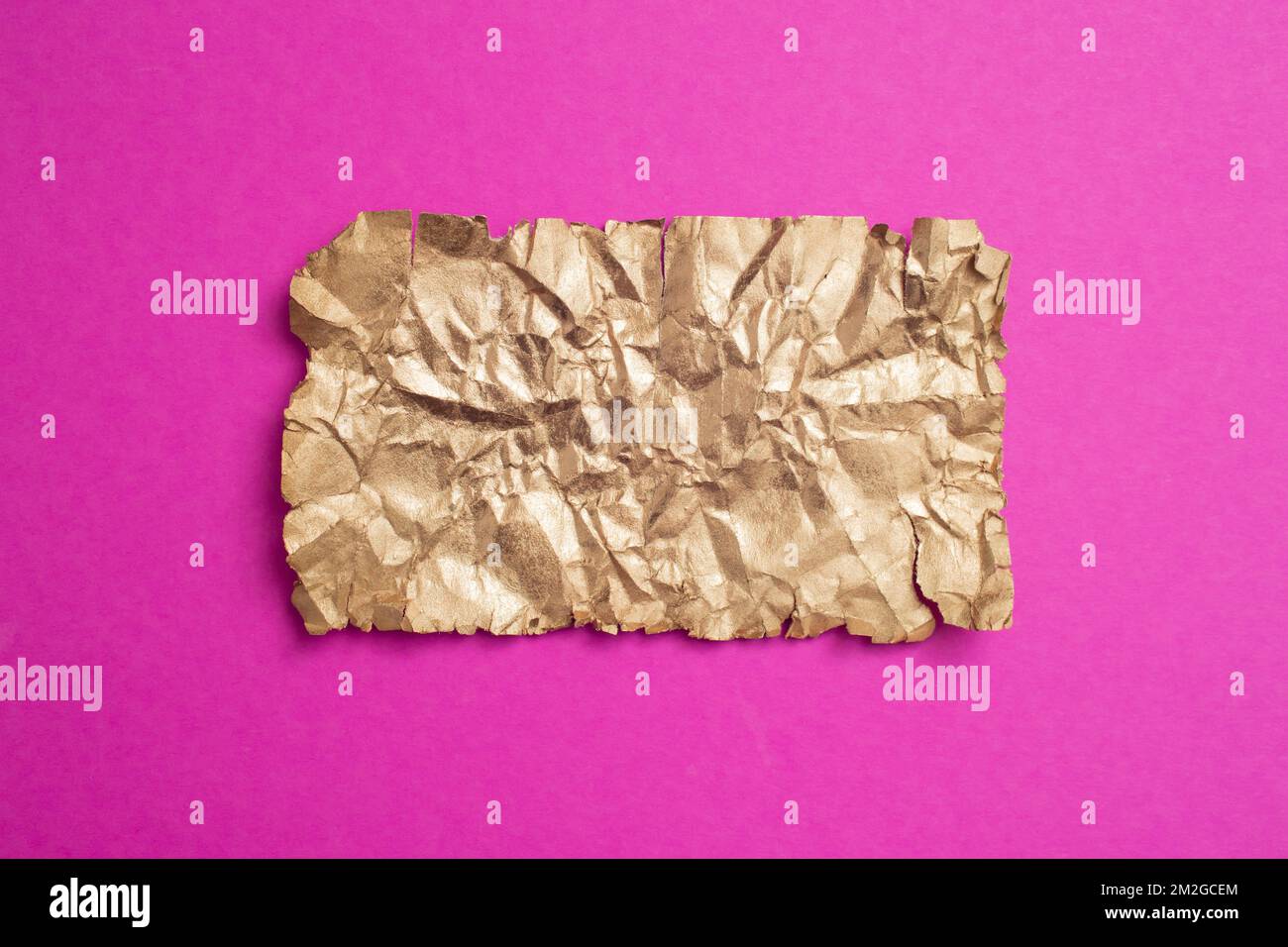 Golden and crumpled paper page on magenta background, soft focus close up Stock Photo
