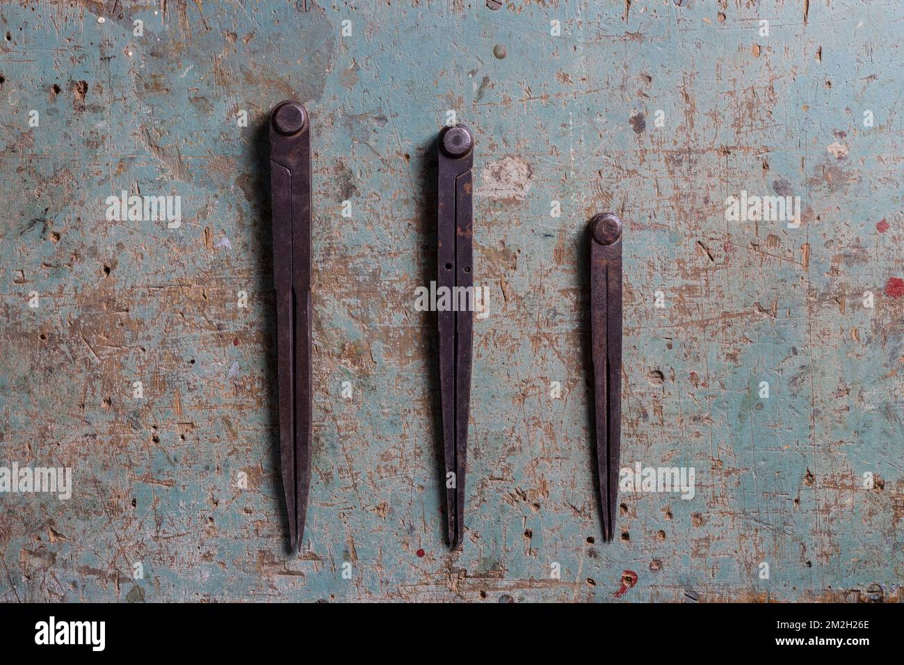 Three metal compass dividers for woodworking on a rustic surface flat