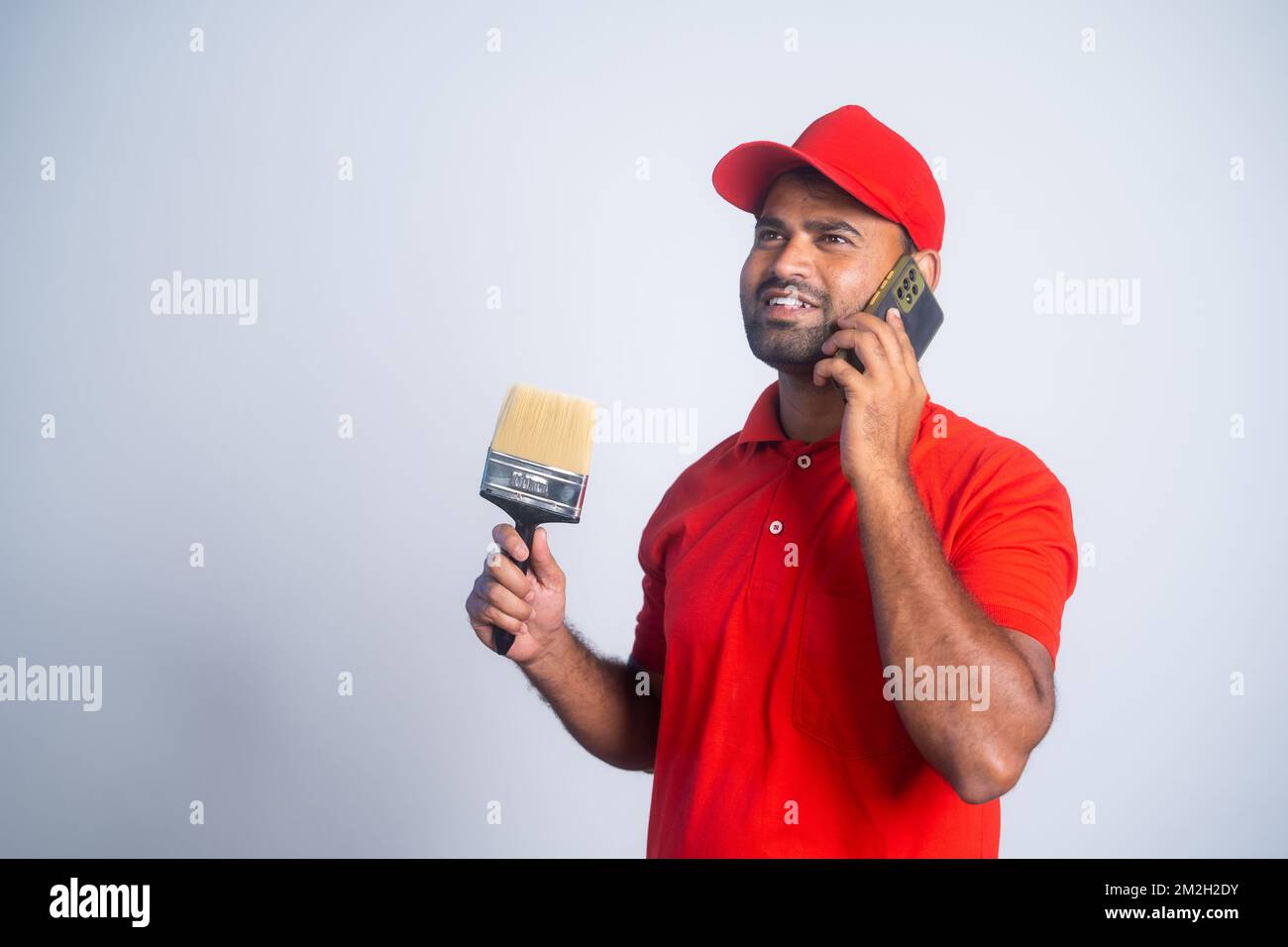 Happy smiling painter man talking on mobile phone by holding brush at apartment - concept of taking break, communication and employment Stock Photo