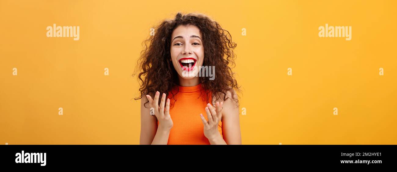 Surprised thrilled and joyful charming european female with curly hairstyle raising palms in grateful and delighted gesture smiling broadly hearing Stock Photo