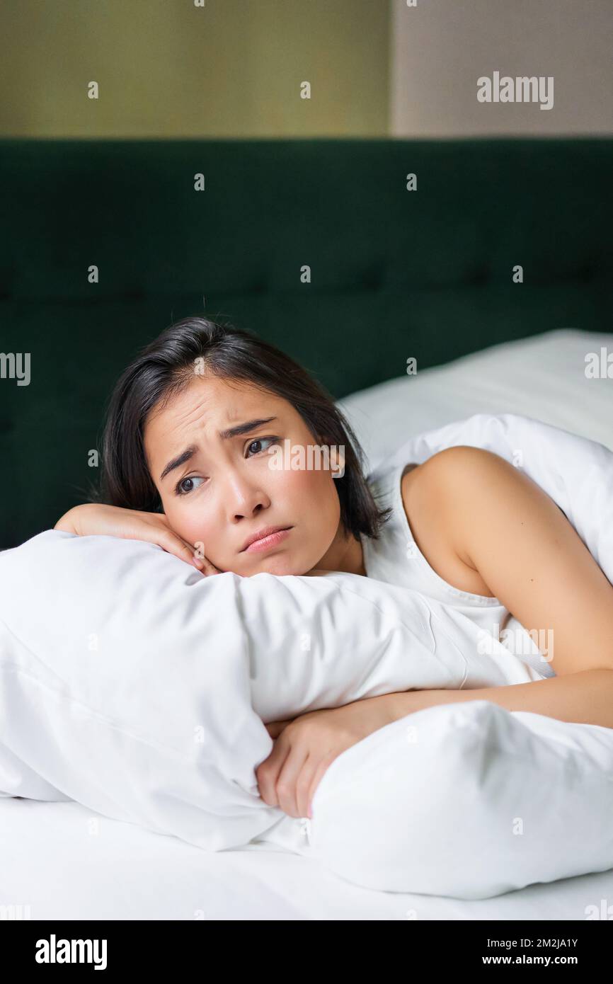 Sad and gloomy asian girl lying in her bed, grimacing and crying
