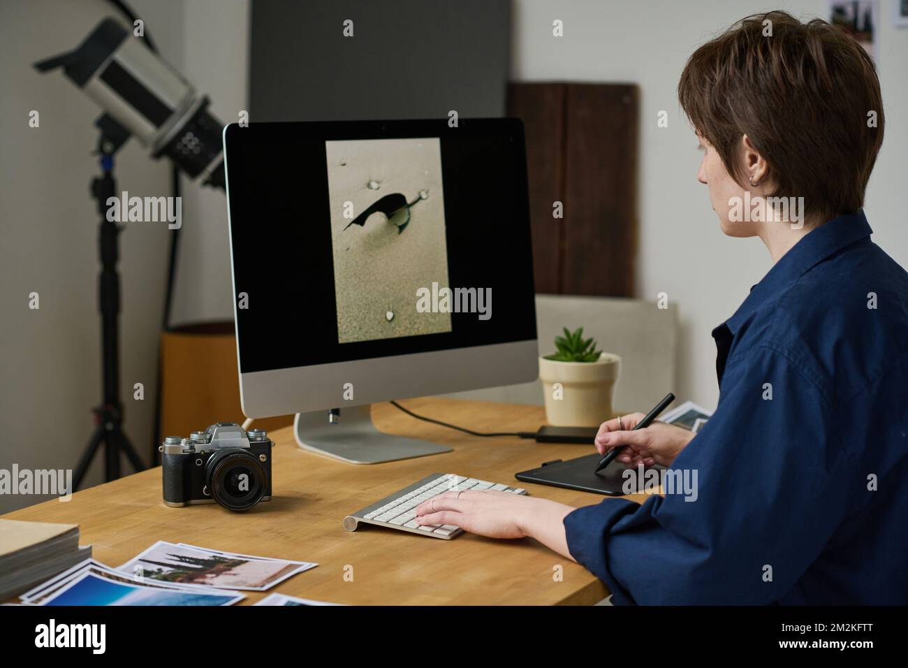 Young graphic designer using digital tablet to retouch photo on computer monitor Stock Photo