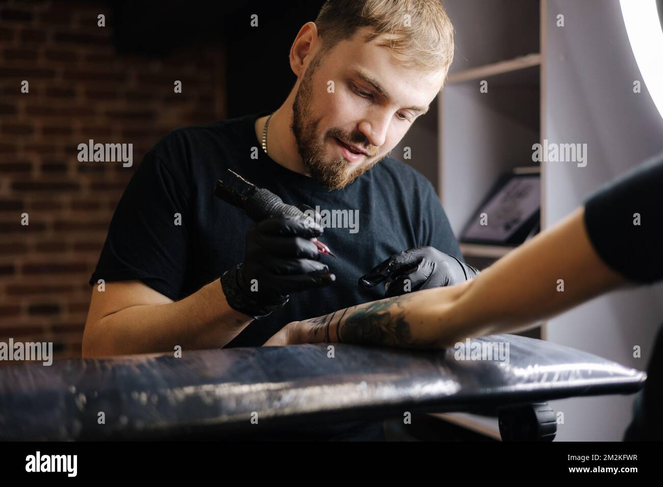 Tattoo master is tattooing a woman's hand. Wireless tattoo machine, safety and hygiene at work. Close-up of tattoo artist work. Tattoo salon Stock Photo