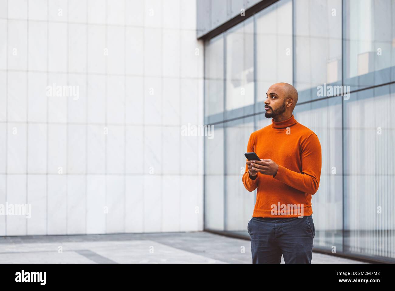Man in orange sweater standing outside with a digital device in his hands Stock Photo