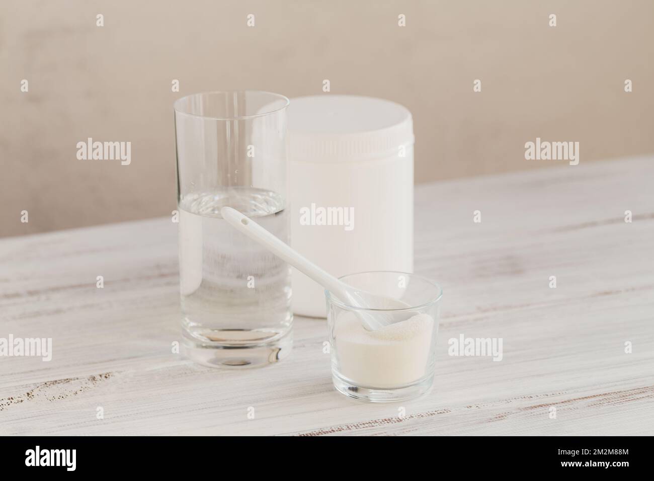 Hydrolyzed marine sourced collagen peptides in glass bowl and water on a white wooden background. Daily supplement concept. Stock Photo