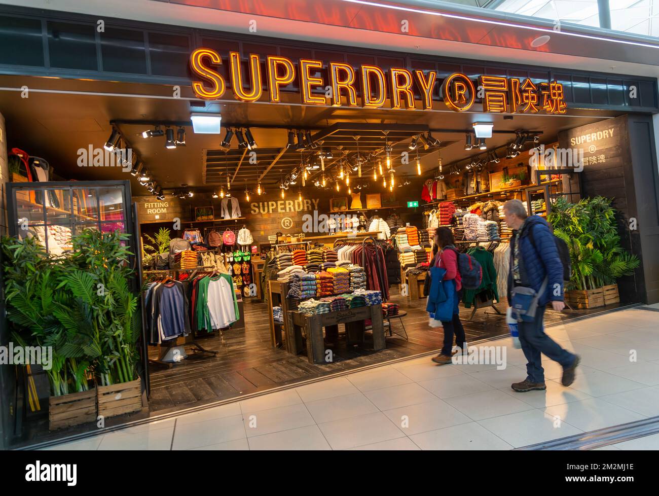 Passengers walking past Superdry clothing fashion shop, Stansted airport, Essex, England, UK Stock Photo