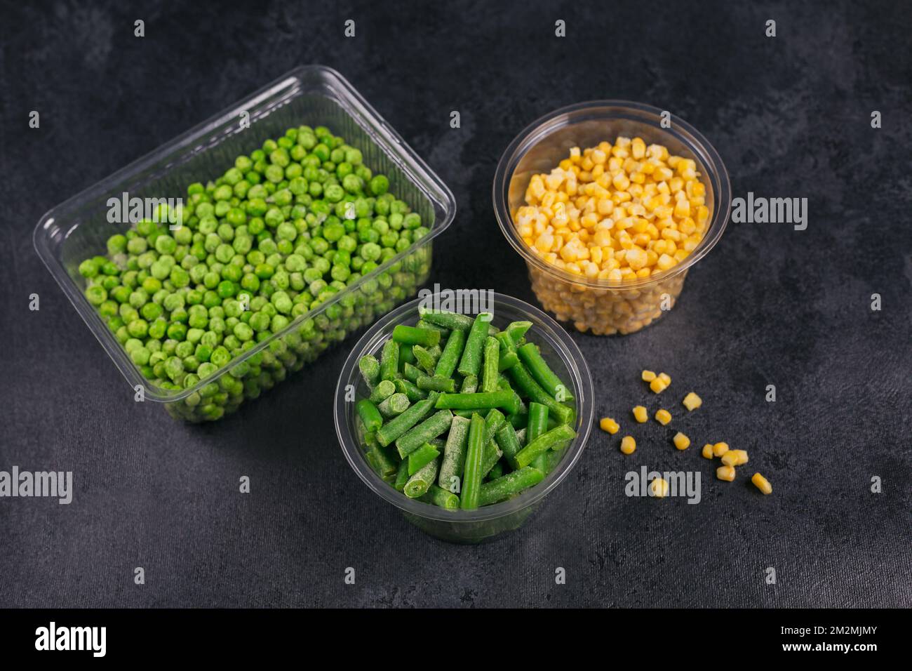 Plastic container with different organic deep frozen vegetables on a black table. Green peas, sweet corn and cut green beans in a box Stock Photo