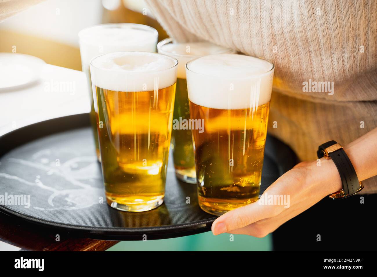Unrecognizable waitress serving three glasses with iced beer with foam on a tray. Stock Photo