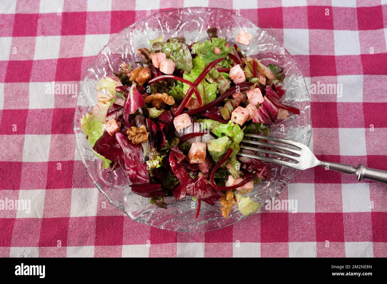 Fresh vegetable salad, lettuce leaf, beetroot, tofu and walnut on glass plate with fork on purple checkered tablecloth. Stock Photo