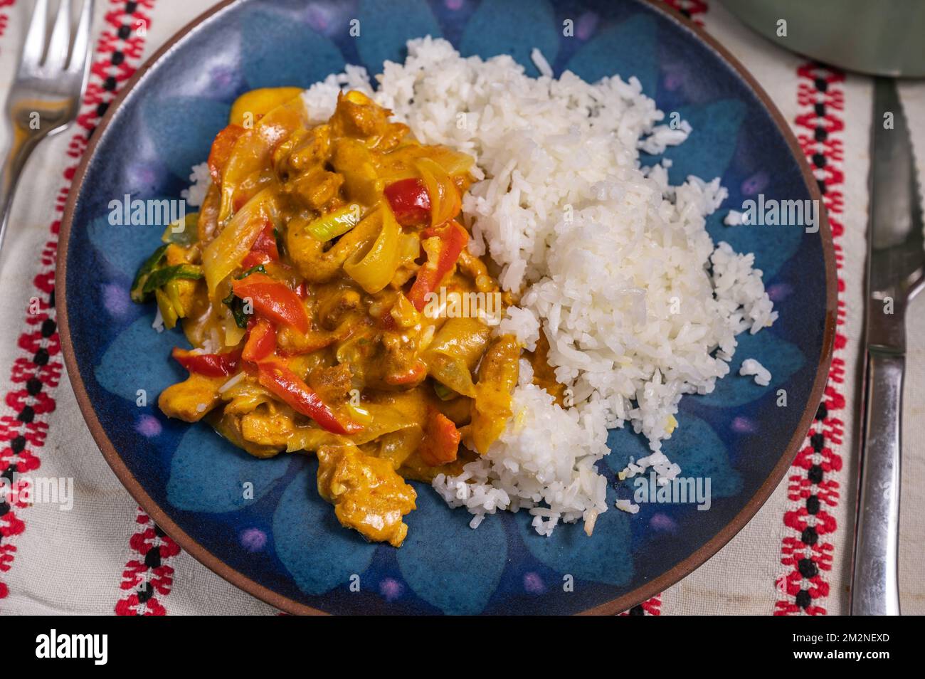 Roasted turkey meat piece with red pepper and onion in soy sauce and coconut milk with rice on blue plate. Asian curry food, closeup. Stock Photo
