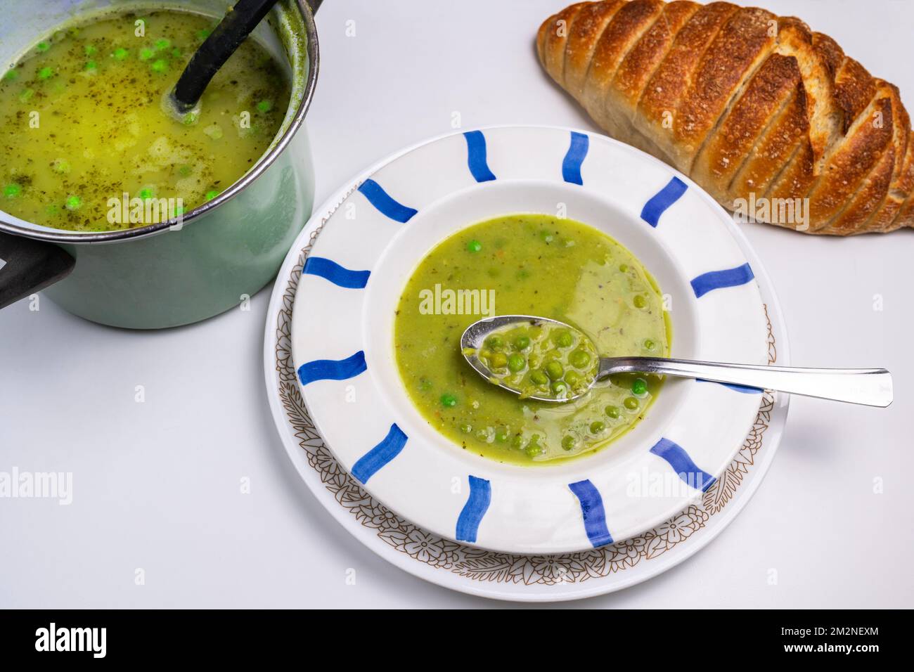 Pea soup in striped plate and pot, spoon and bread on white background. Stock Photo