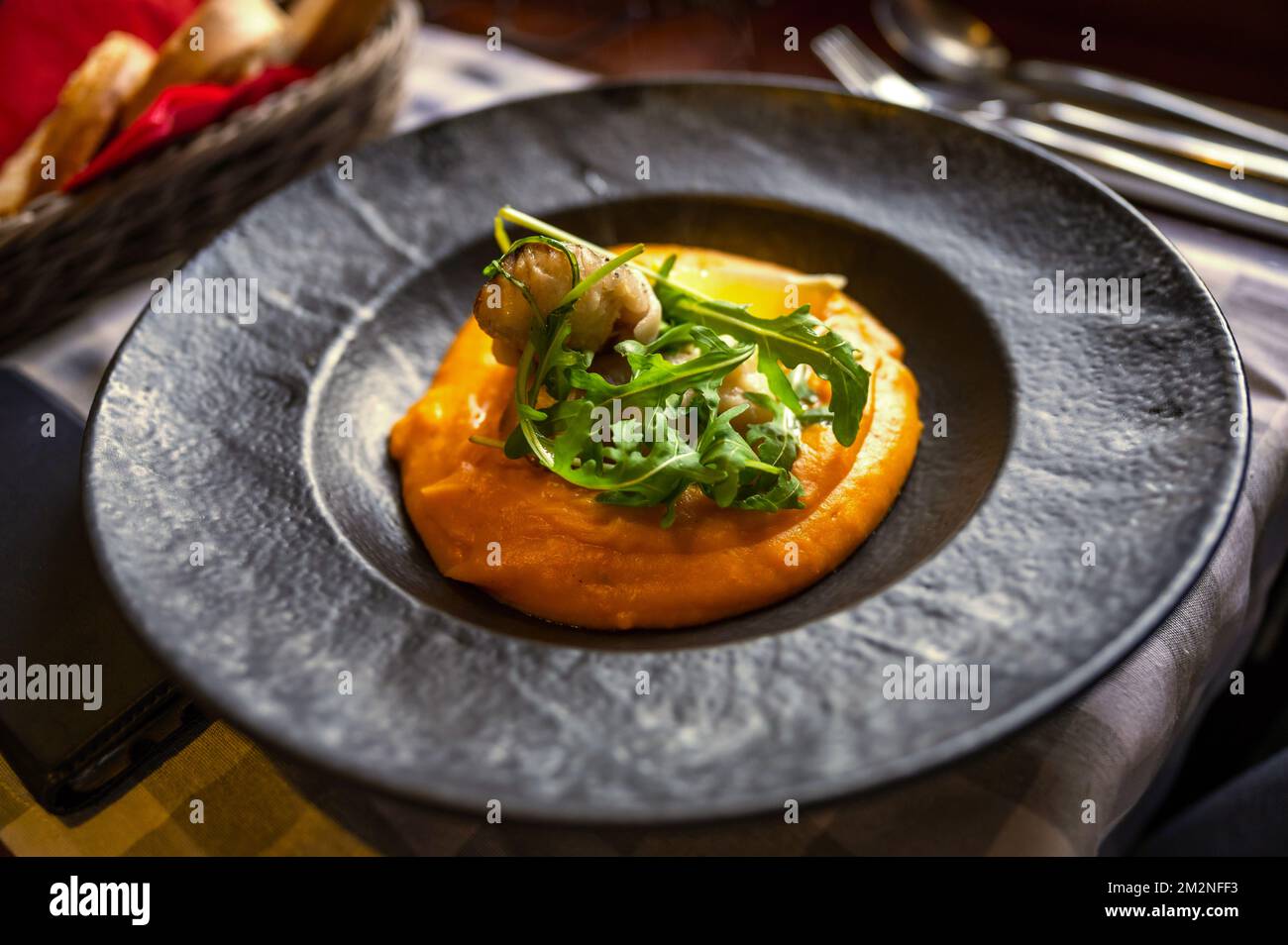 Zander fillet with fried bacon on pumpkin puree, rucola leaf in plate on restaurant table, closeup. Stock Photo