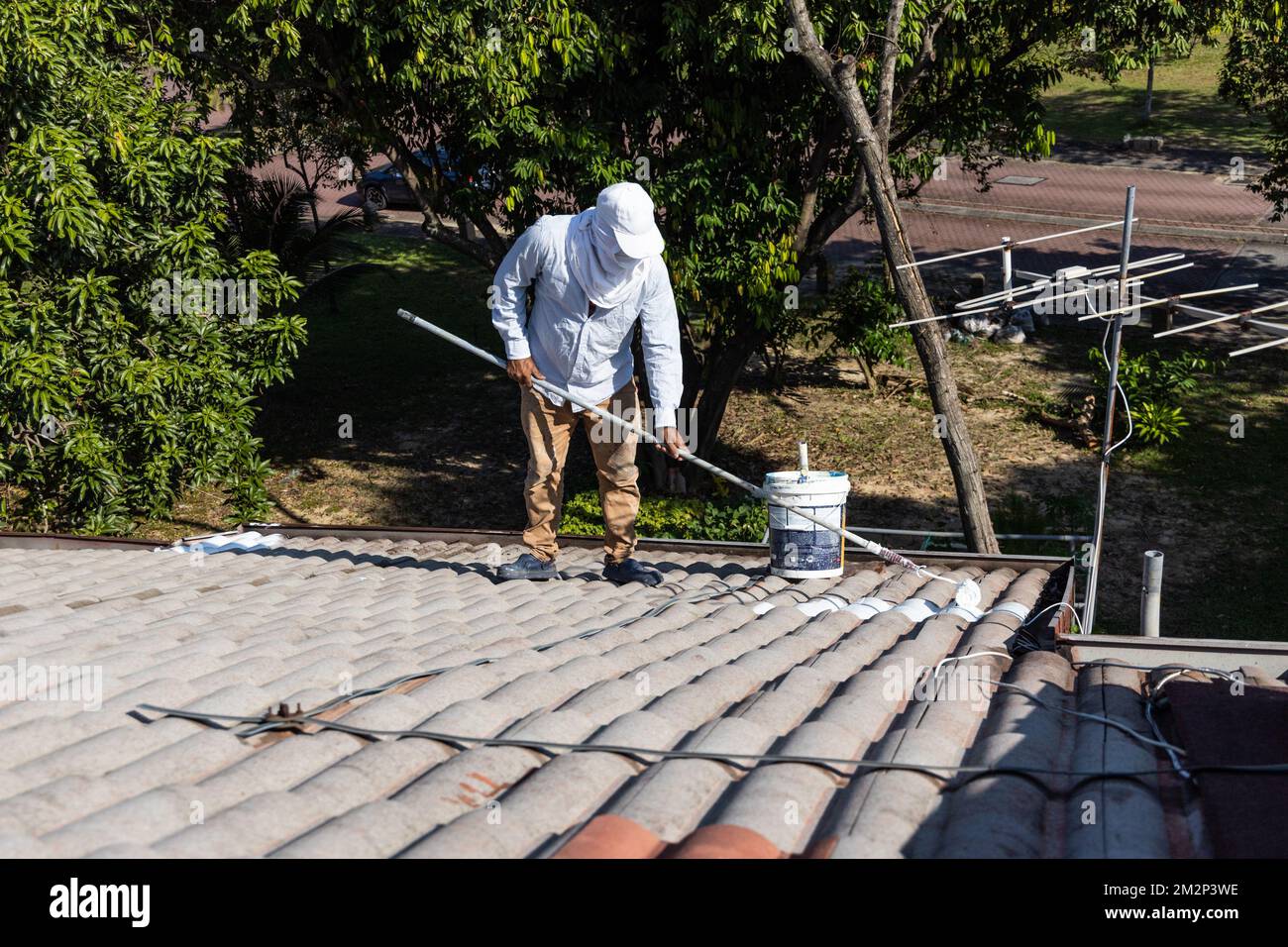Worker adding undercoat foundation paint onto rooftop with roller at
