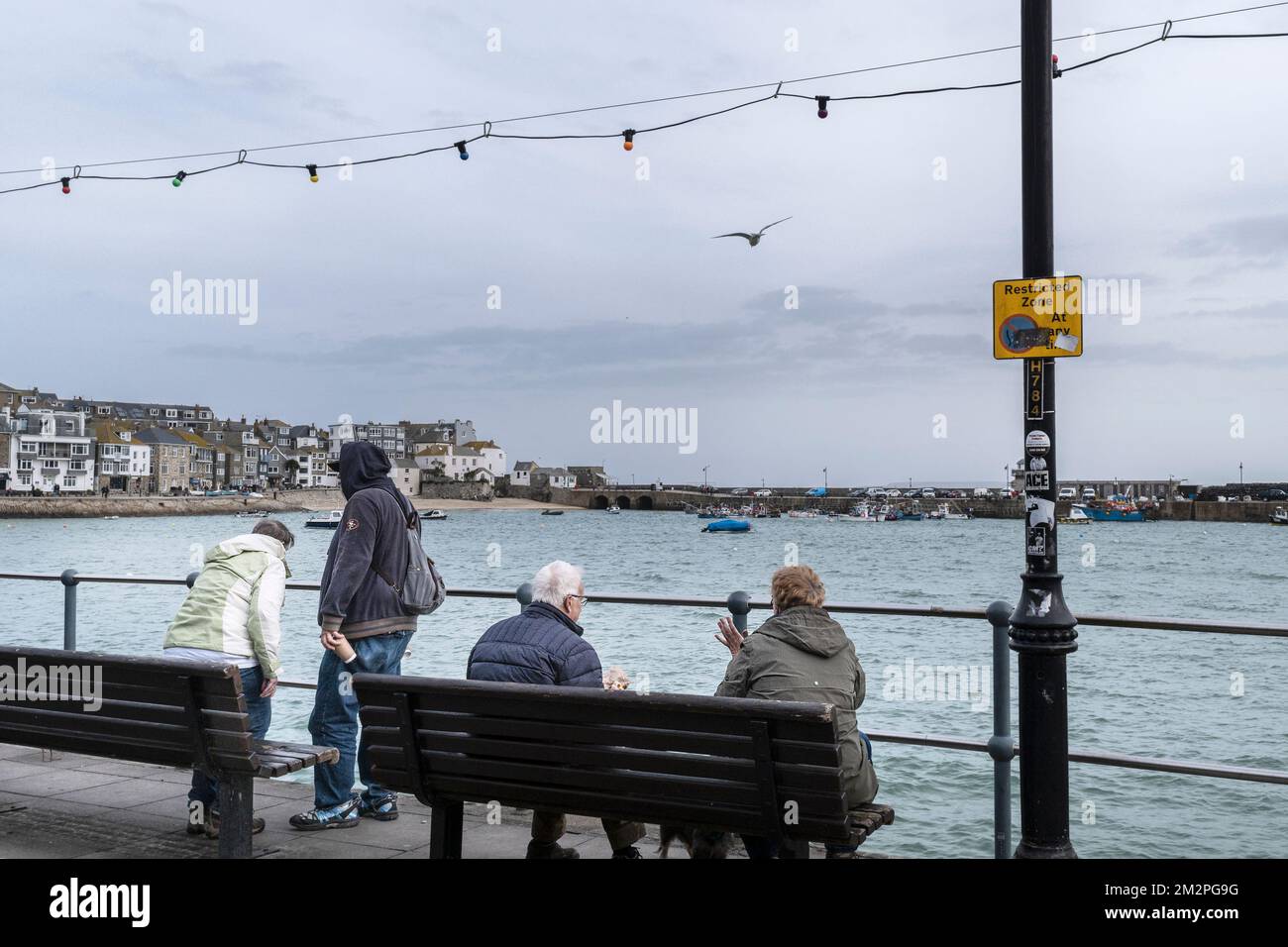 UK weather. Visitors sitting on a bench looking out over the harbour to Smeatons Pier on a rainy chilly miserable day in the historic seaside town of Stock Photo