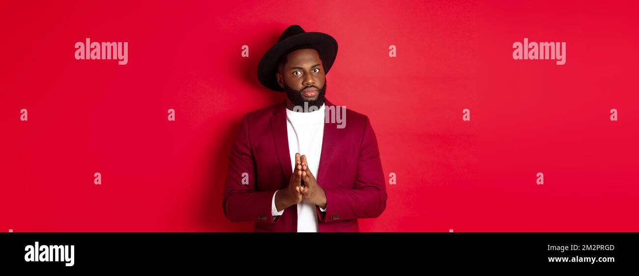 Serious looking man getting ready to business, holding hands pressed together and nervously staring at camera, listening closely, standing against red Stock Photo